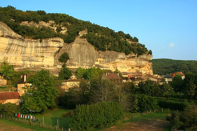 The limestone cliff above the village of Les Eyzies in the Vézère valley, with houses at its foot in warm late-afternoon light