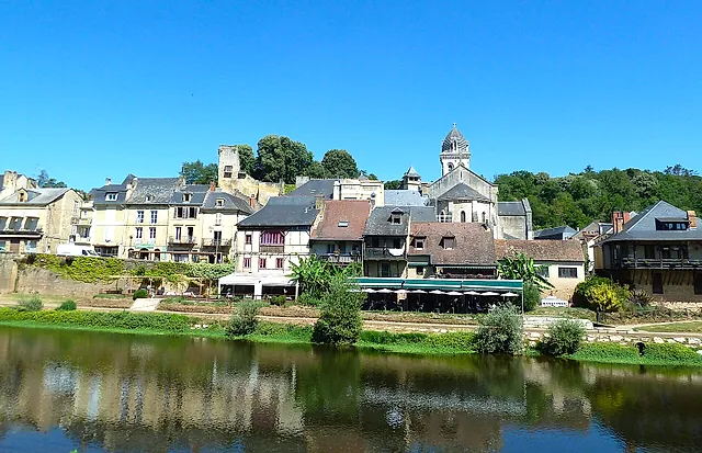 Old houses, the ruined castle tower and the church bell tower of Montignac above the Vézère, reflected in the water under a blue sky