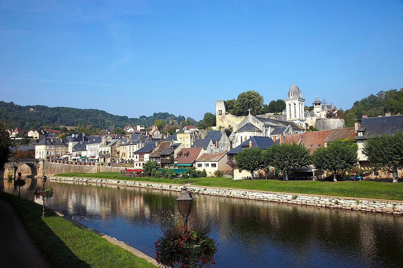 Montignac seen from the banks of the Vézère, with the church bell tower and old houses along the river under a clear blue sky