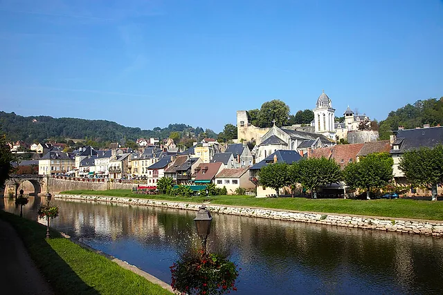 Montignac seen from the banks of the Vézère, with the church bell tower and old houses along the river under a clear blue sky