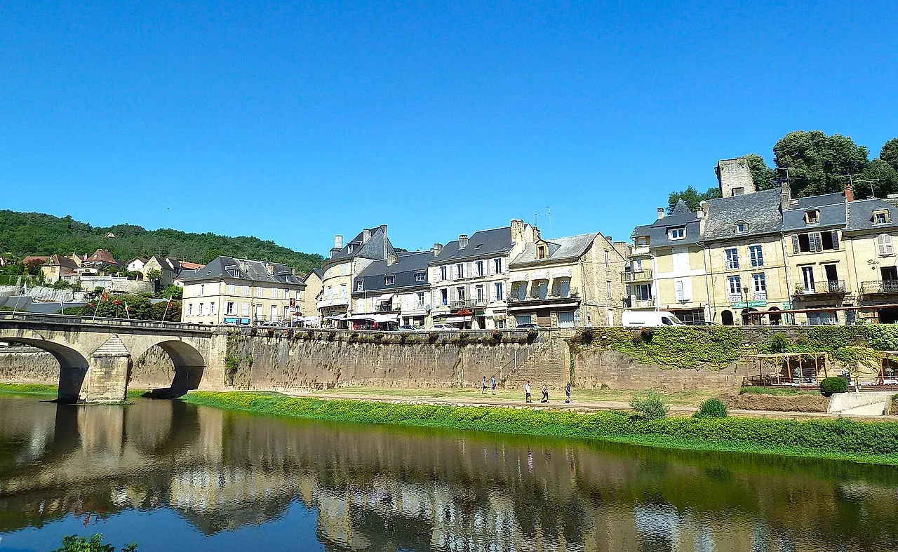 The stone bridge over the Vézère at Montignac and the riverside houses reflected in the calm water under a blue sky