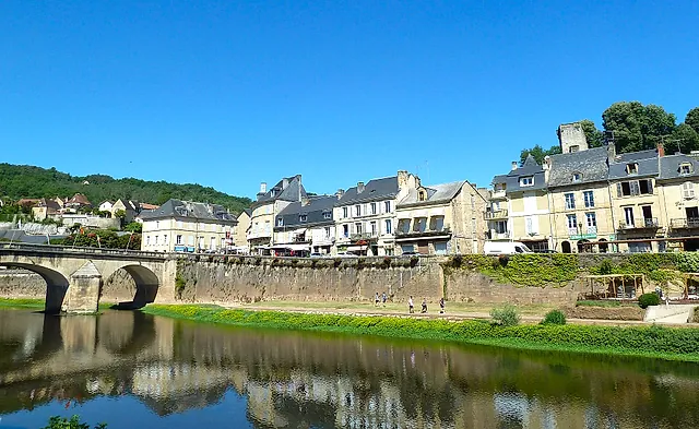 The stone bridge over the Vézère at Montignac and the riverside houses reflected in the calm water under a blue sky