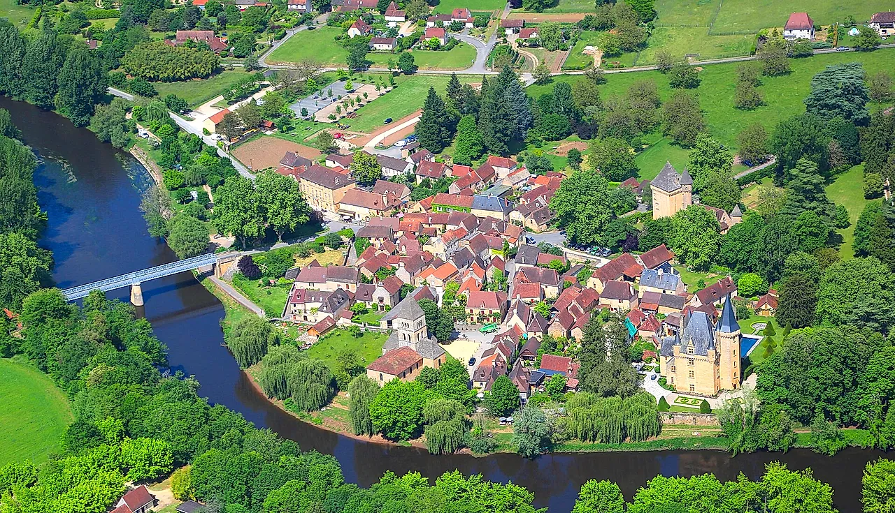 Aerial view of the village of Saint-Léon-sur-Vézère in a bend of the Vézère river, with its bridge, church and château among green fields