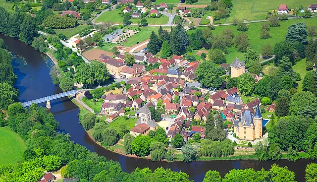 Aerial view of the village of Saint-Léon-sur-Vézère in a bend of the Vézère river, with its bridge, church and château among green fields