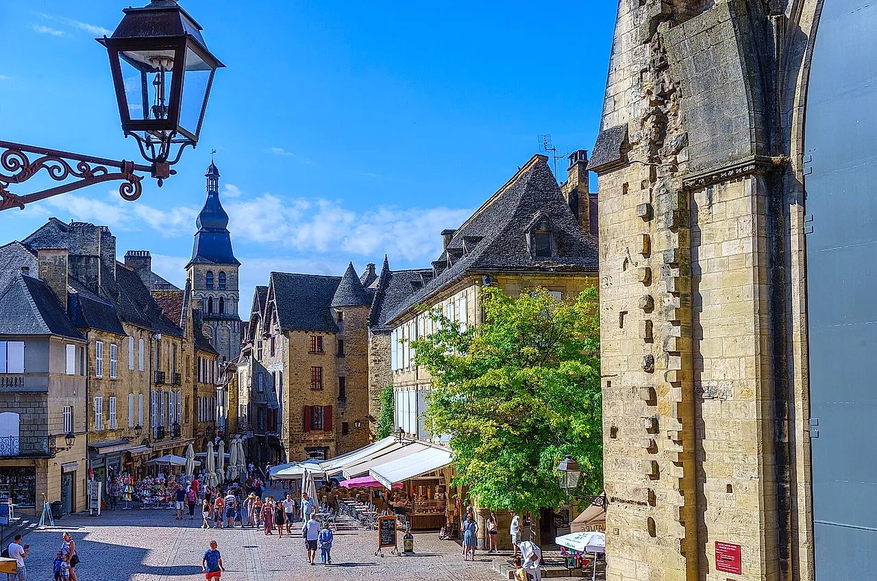 Place de la Liberté in Sarlat-la-Canéda, with honey-coloured stone houses, a bell tower in the distance and a wrought-iron lantern, under a blue sky