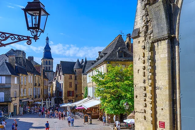 Place de la Liberté in Sarlat-la-Canéda, with honey-coloured stone houses, a bell tower in the distance and a wrought-iron lantern, under a blue sky