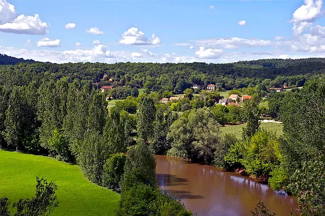 The Vézère winding through green meadows and woods in the Périgord, seen from La Roque Saint-Christophe, under a sky with white clouds